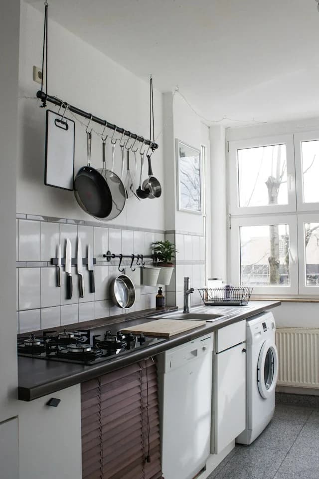 A bright kitchen with a gas hob, a dishwasher and a washing machine under a rail of hanging pans