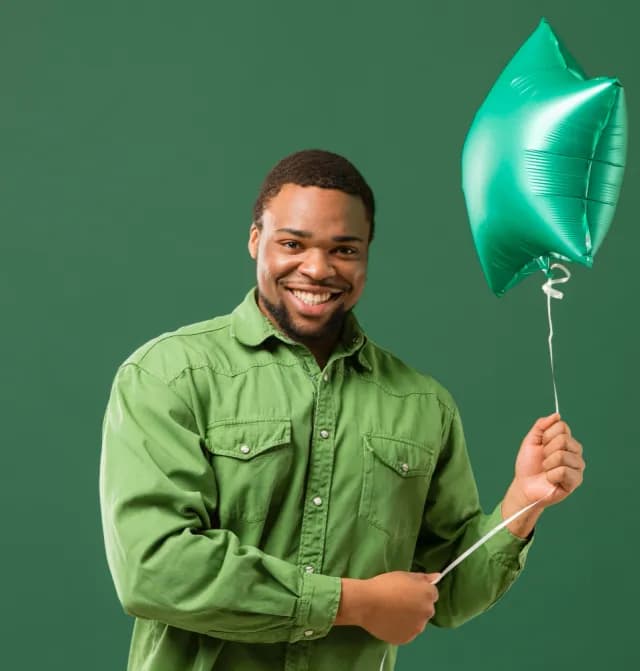 A smiling man in a green shirt holding a green star-shaped balloon