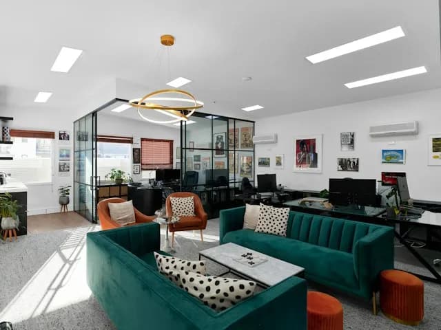 A bright open-plan office with green velvet sofas, orange armchairs and glass-walled workspaces