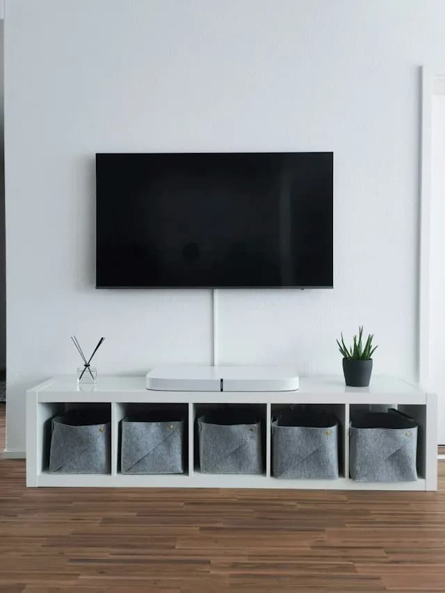 A wall-mounted flat-screen TV above a white console with grey storage baskets