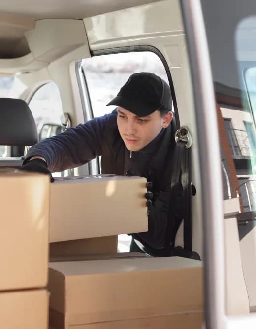 A driver in a black cap stacking cardboard boxes in the back of a van